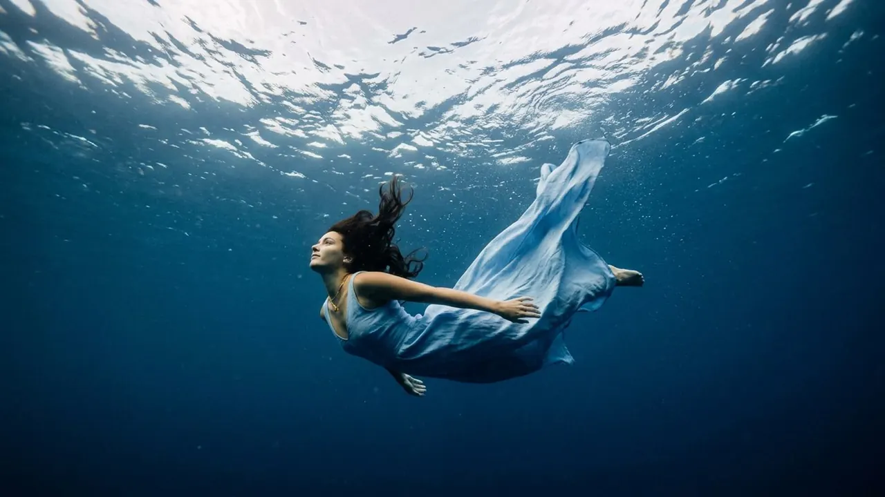 Blue Depth: The subject sits submerged in deep blue water with light above.